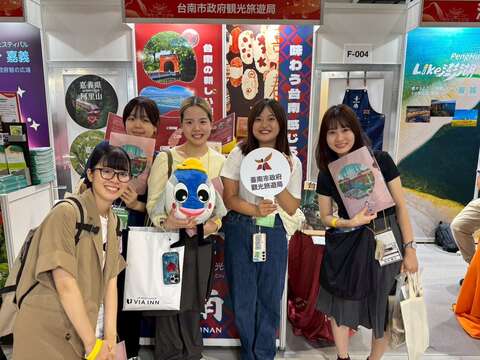 日本旅展现场，参观民众与台南市政府观光旅游局文宣品及展物合影，展现对台南观光的热情支持