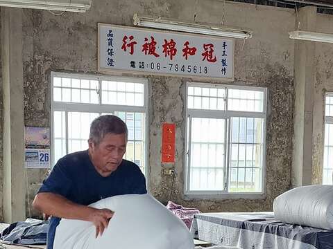 蔡顺龙在铺好的棉花放上防沾布,套上内胎被套,从角落往中间折後,再快速翻出及整型。(郑佩雯拍摄)
