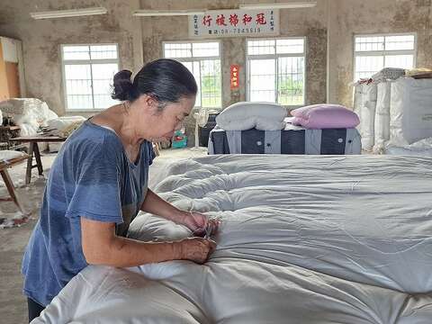 冠和的老师傅挥汗工作,将内胎被套与棉花缝合固定,从角落下针逐渐往内,双人被一共需61针,缝合点不管从哪个角度看都呈直线,全凭经验,无需丈量。(郑佩雯拍摄)