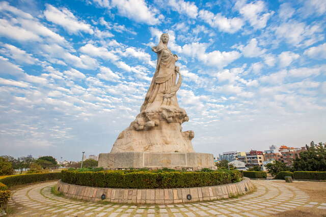 The statue of Lin Mo Niang stands tall in the center of the flower bed in the park.